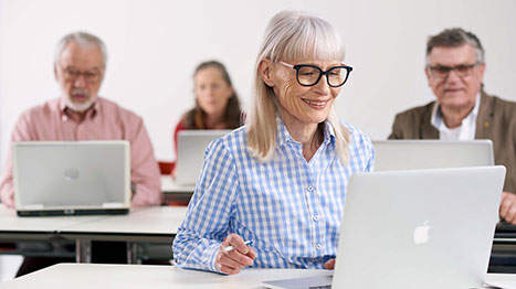 Eine ältere Frau mit Brille sitzt in ihrem Arbeitszimmer am Computer