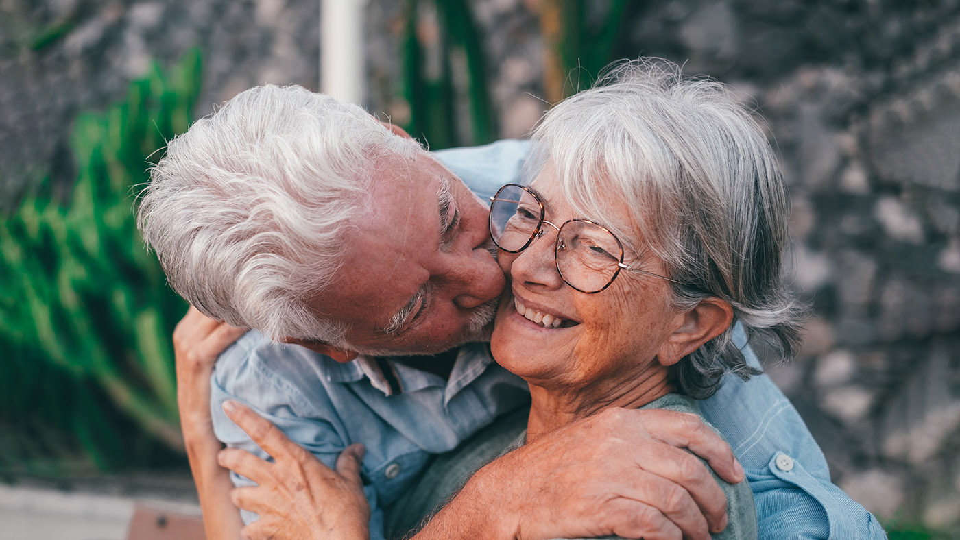 Ein Senior küsst seine Frau auf die Wange und umarmt sie